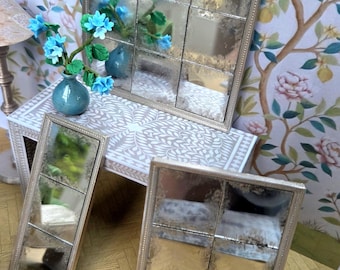 May include: Three antique-style mirrors with silver frames. The largest mirror is square and divided into nine sections. A smaller rectangular mirror and a square mirror are also present. A small blue vase with blue flowers sits on a table in the background.