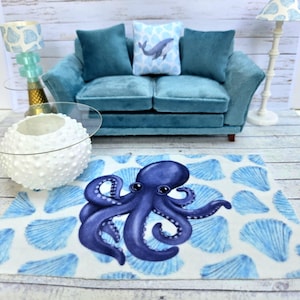Puede incluir: Una escena de sala de estar en miniatura con un sofá turquesa, cojines y una alfombra con un diseño de pulpo azul. También se ven un jarrón decorativo blanco y una lámpara con una pantalla azul estampada. La alfombra tiene un patrón de conchas marinas.