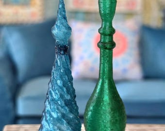 May include: Two decorative bottles with pointed stoppers. One bottle is a translucent blue with a spiraled, textured surface. The other bottle is a solid, metallic green with a smooth, rounded base and a slender, elongated neck design.