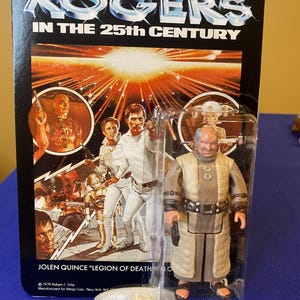 Puede incluir: Una taza de cerámica blanca con un asa negra y el texto "But First, Coffee" en negrita negra. La taza está sobre una superficie de madera. La taza mide aproximadamente 10 cm de alto.