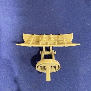 Può includere: Un modello in plastica beige di un'arma d'assedio medievale, un trabucco, con un braccio sollevato e una ruota alla base.
