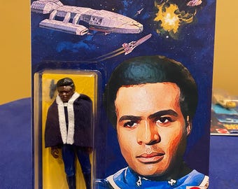 Può includere: Una action figure vintage del Colonnello Tigh della serie televisiva Battlestar Galactica. La figura indossa un'uniforme blu con colletto bianco e un mantello nero. La figura è confezionata in una confezione blister di plastica con sfondo giallo e un'immagine del Colonnello Tigh sul davanti. La confezione include anche il testo "Battlestar Galactica" e "Colonel Tigh".