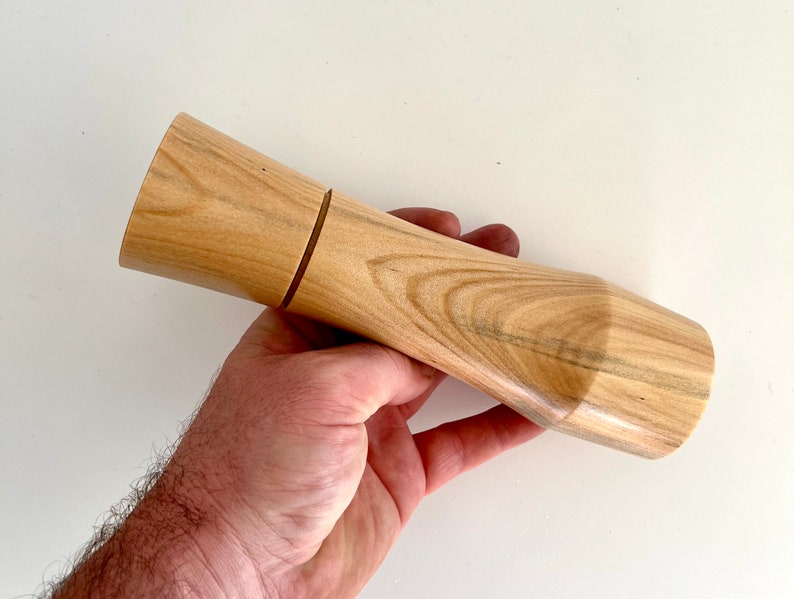 Mans hand holding single curved tapered Norfolk island pine grinder