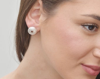Puede incluir: Pendientes de botón de plata con forma de erizo de mar. Los pendientes son pequeños y delicados, y tienen una superficie texturizada.