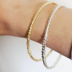 Könnte beinhalten: Zwei Armreifen, einer in Gold und einer in Silber, mit einem strukturierten, perligen Design.