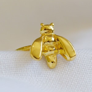 May include: A gold-colored ring with a bee design. The bee is detailed with wings, a body, and a head.