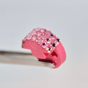 May include: A pink plastic charm with a row of pink rhinestones.