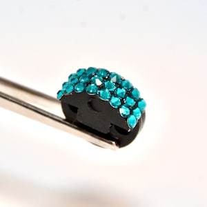 May include: A small, black, round, plastic object with a row of turquoise rhinestones around the edge.