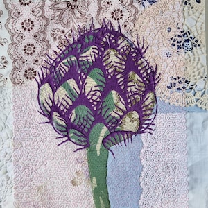 Könnte beinhalten: Ein gesticktes Artischocken-Design in Lila und Grün auf einem Patchwork aus weißem Stoff mit Spitzenbesatz.