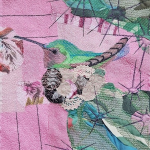 Puede incluir: Pieza de arte textil que representa un colibrí con plumas verdes y azules, posado cerca de un grupo de flores. El fondo es rosa con líneas verticales. La obra de arte incorpora varias texturas y telas.