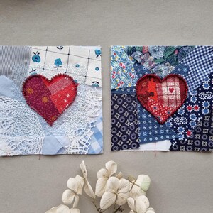 May include: Two handmade patchwork squares featuring red hearts at their centres. The squares are crafted from various fabrics in shades of blue, white, and red. The hearts are constructed from red and white fabric and are stitched together with red thread.
