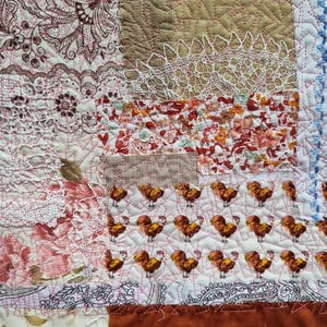 Könnte beinhalten: Nahaufnahme eines Patchwork-Textils mit verschiedenen Stoffmustern. Es umfasst florale Drucke, Spitze und ein sich wiederholendes Hahn-Motiv. Die Farbpalette besteht aus Rot-, Braun- und Cremetönen, mit sichtbaren Nähten.