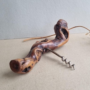 Könnte beinhalten: Ein Korkenzieher mit einem Griff aus einem Stück poliertem, knorrigem braunem Holz mit natürlicher, unregelmäßiger Form. Eine silberfarbene Metallspirale ist in der Mitte des Holzgriffs befestigt und erstreckt sich nach rechts.
