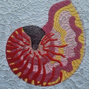 May include: An embroidered nautilus shell design in red, pink, yellow, and black. The shell is set against a light blue lace background. The artwork showcases detailed embroidery. The design is a colorful and textured piece of art.