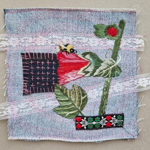 Può includere: Una piccola opera d'arte ricamata con un fiore rosso con foglie verdi, un'ape e un motivo a scacchi bianco e nero su tessuto denim.