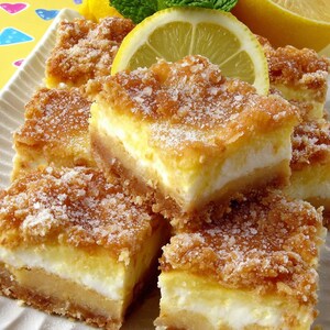 Peut inclure: Une assiette de barres au citron avec une garniture émiettée, garnie de tranches de citron et de feuilles de menthe. Les barres ont un aspect en couches avec une croûte brun doré, une garniture blanche crémeuse et une garniture sucrée.