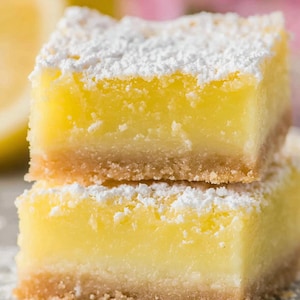 Puede incluir: Dos barras de limón apiladas. Tienen una base dorada y mantecosa y un relleno cremoso amarillo brillante. Azúcar glas espolvoreado por encima, creando un dulce y delicioso postre.