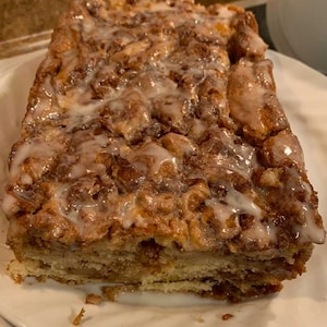 Könnte beinhalten: Nahaufnahme eines Zimtschneckenbrotes, das mit einem weißen Zuckerguss überzogen ist. Das Brot liegt auf einem weißen Teller.