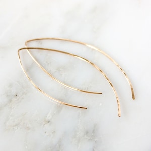 May include: A pair of gold-toned, hammered, thin, wire earrings in the shape of a long, narrow oval.