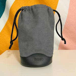 May include: Gray drawstring lens pouch with a black leather bottom and the word "Canon" embossed on the front.