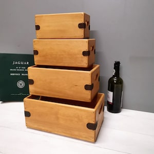 May include: Four wooden boxes stacked on top of each other. The boxes are made of light wood and have metal hinges. The boxes are all the same size and shape. The boxes are sitting on a white surface.