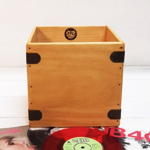 Op de afbeelding: Een houten doos met metalen hoekaccenten. De doos is lichtbruin en heeft een sticker op de bovenkant met de tekst "Apple Records".