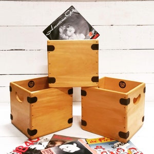 Op de afbeelding: Drie houten opbergdozen voor platen met zwarte metalen accenten. De bovenste doos heeft een vinylplaat met de titel "American Girl" erop.