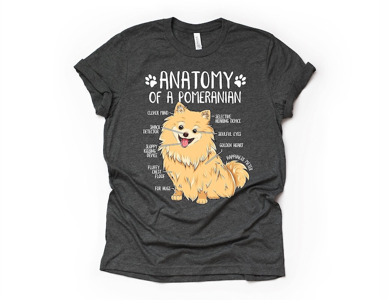 Op de afbeelding: Een grijs T-shirt met een witte afbeelding van een dwergspits. De afbeelding is voorzien van de tekst "Anatomie van een dwergspits" en bevat humoristische anatomische kenmerken zoals "Slimme Geest", "Slordig Kusapparaat" en "Pluche Borstpluis".