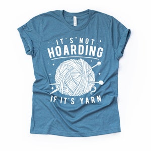 May include: A blue t-shirt with a white graphic that says "It's not hoarding if it's yarn" with a drawing of a ball of yarn and knitting needles.