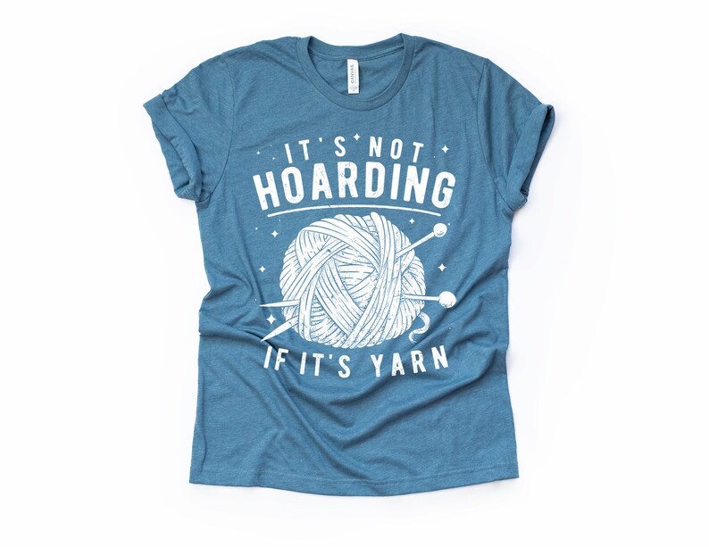 May include: A blue t-shirt with a white graphic that says "It's not hoarding if it's yarn" with a drawing of a ball of yarn and knitting needles.