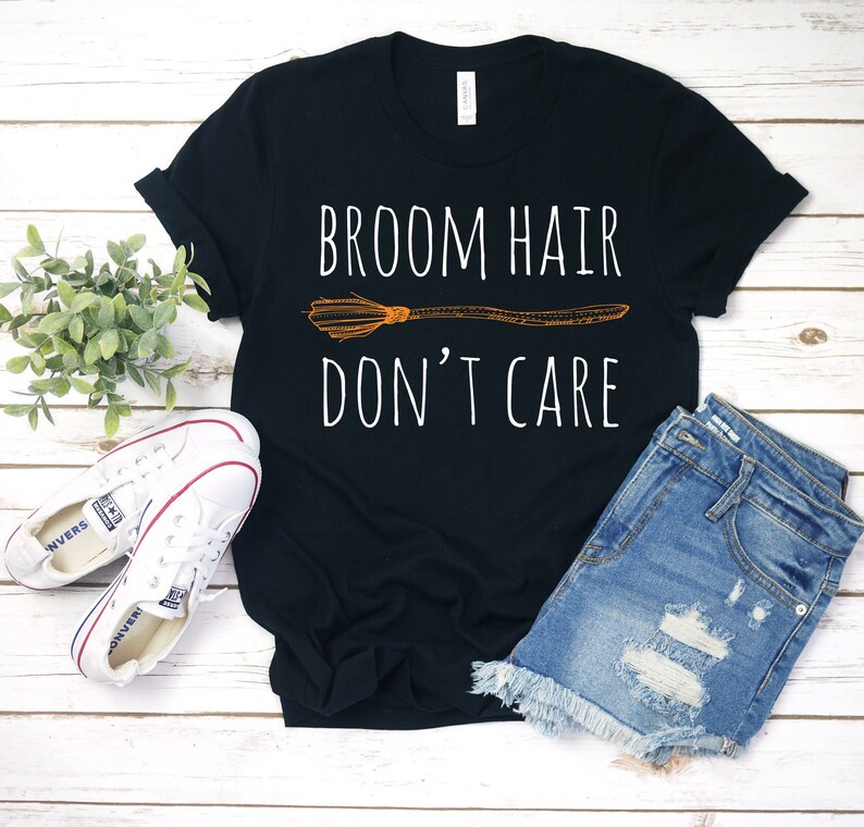 May include: Black t-shirt with the text "BROOM HAIR DON'T CARE" in white, and a broom graphic in orange. The shirt is paired with denim shorts and white sneakers, suggesting a casual, everyday style.