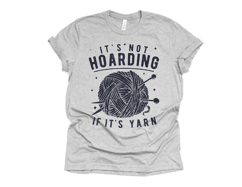 May include: Gray t-shirt with a blue graphic of a ball of yarn and knitting needles. The text on the shirt reads "It's not hoarding if it's yarn."