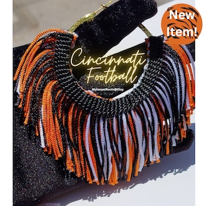 Op de afbeelding: Cincinnati Football oorbellen met zwarte, oranje en witte franjes. De goudkleurige oorringen hebben de tekst "Cincinnati Football". Een "New Item!" sticker staat rechtsboven.