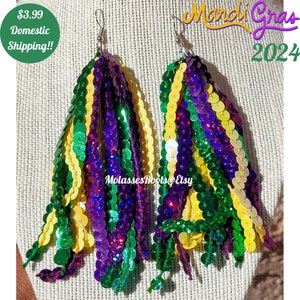 May include: A pair of Mardi Gras themed earrings with green, purple, and gold sequins. The earrings are made of multiple strands of sequins that are tied together at the top.