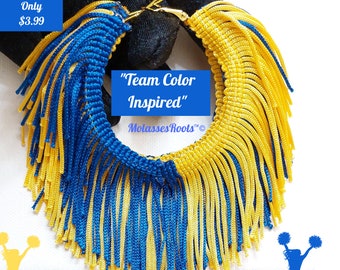 Pode incluir: Um par de brincos de argola dourados com franjas azuis e amarelas. Os brincos são etiquetados como "Team Color Inspired" e "MolassesRoots™".