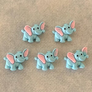 May include: Five light blue plastic elephant buttons with pink ears. The elephants are facing forward with their trunks raised.