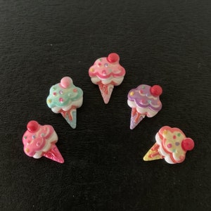 May include: Five colorful ice cream cone shaped charms with pink, purple, green, and white frosting and sprinkles.
