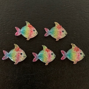 May include: Five rainbow glitter fish with red flowers on their heads. The fish are made of resin and have a glossy finish.