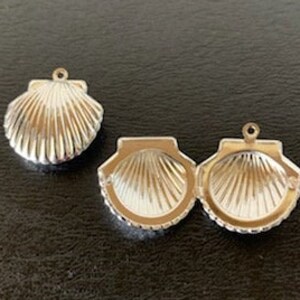May include: Two silver-toned seashell charms. One charm is a single seashell, the other is a hinged seashell charm that opens.