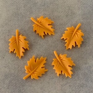 May include: Five small, orange, plastic leaves with a detailed design. The leaves are arranged in a circle on a light gray surface.