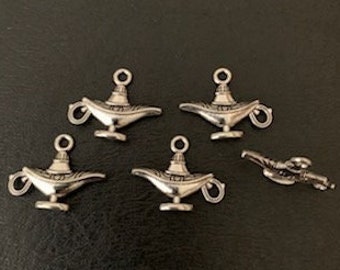 May include: Six silver genie lamp charms with a detailed design. The charms have a loop at the top for attaching to jewelry or other crafts.
