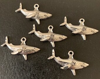 May include: Five silver shark charms with a detailed design. The charms are about 1 inch long and have a loop at the top for attaching to jewelry.