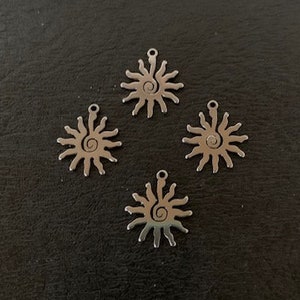 May include: Four silver metal sun charms with a swirl design. The charms are on a dark gray background.