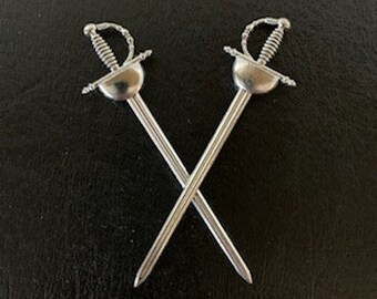 May include: Two silver sword-shaped cocktail picks crossed over each other.