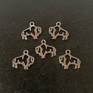 May include: Five silver-colored buffalo charms. Each charm is a cutout of a buffalo silhouette with a small loop at the top for attaching to jewelry or other crafts. The charms are displayed on a dark surface.