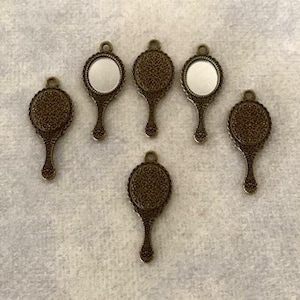 May include: Six antique gold-toned hand mirrors with ornate detailing. The mirrors are round and have a small loop at the top for hanging.