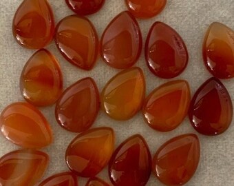 May include: A collection of 20 teardrop-shaped carnelian gemstones. The stones are a deep orange color with white striations. They are perfect for jewelry making or other craft projects.