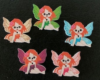 May include: Five wooden fairy ornaments with wings, each with a different color scheme. The fairies have red hair, pink, blue, green, and orange wings, and are wearing dresses.