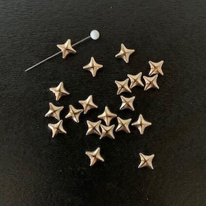 May include: A collection of gold-colored star-shaped metal studs, scattered on a black surface.