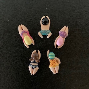 May include: Six small ceramic figurines of people in swimming poses. Each figurine is painted with different colors and patterns. The figurines are on a black background.